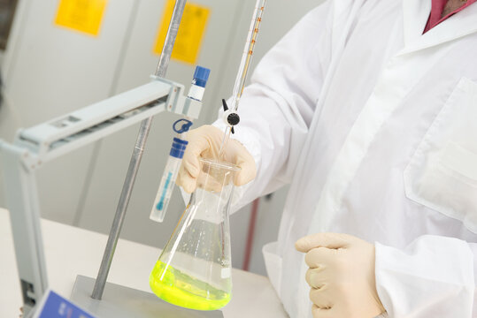 Unrecognizable chemist in protective gloves and uniform standing in laboratory and pouring liquid reagents into flask