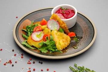 Fried french fries breaded with greens, radishes and beet chips on a white plate.