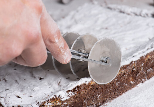 Closeup from above of crop faceless person using stainless steel pastry cutter while cutting delicious brownie with tender texture and decorated with powdered sugar