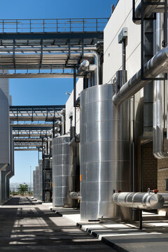Asphalt walkway going through contemporary factory with metal tanks on background of blue sky