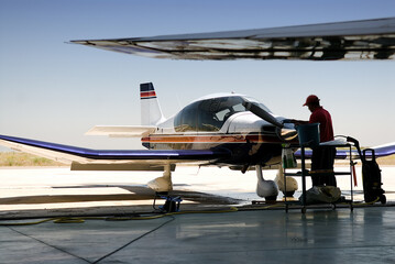 Side view of male employee in uniform cleaning jet airplane while standing on airfield during sunny day