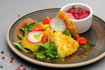 Fried french fries breaded with greens, radishes and beet chips on a white plate.