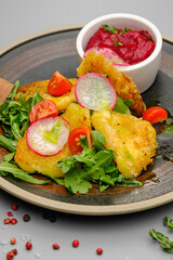 Fried french fries breaded with greens, radishes and beet chips on a white plate.