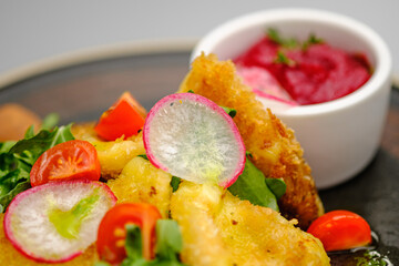 Fried french fries breaded with greens, radishes and beet chips on a white plate.