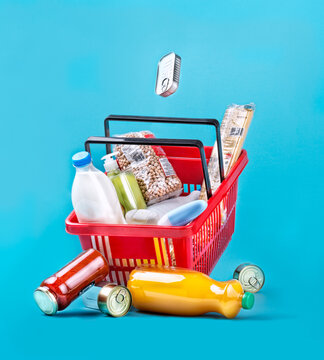 Red plastic shopping basket with fresh groceries in packages placed on light blue background in studio