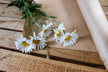 Obraz na płótnie Canvas white flowers on a wooden table with a roll of craft paper with a white background in the interior, chamomile