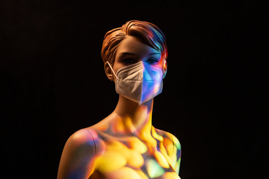 Plastic female mannequin in medical mask illuminated by colorful lights in studio on black background
