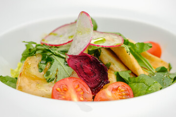 Squid with vegetables, tomatoes, salad and radishes on a white plate.