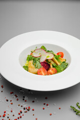 Squid with vegetables, tomatoes, salad and radishes on a white plate.