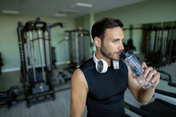 Young athletic man having water break while working out in a gym.