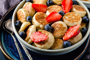 Mini cereal pancakes with strawberries and blueberries in boul on blue cement background, top view. Horizontal format