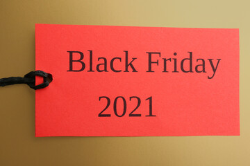 Red tag with words BLACK FRIDAY 2021 on golden background, top view