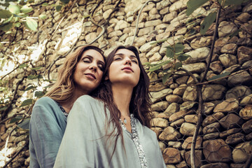 From below of charming young daughter and slender middle aged mother hugging tenderly in green garden in summer