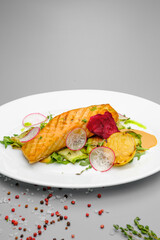 Grilled salmon steak with vegetables on a white plate.