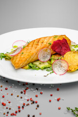 Grilled salmon steak with vegetables on a white plate.