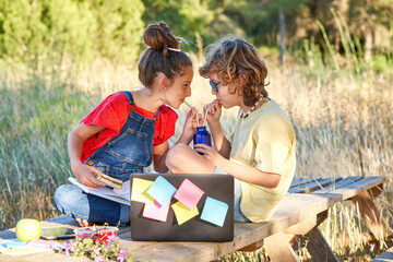 A ten-year-old boy and girl in the field sharing a drink in a bottle with some straws