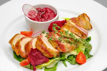 Chicken fillet in bacon with arugula and sauce on a white plate.