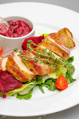 Chicken fillet in bacon with arugula and sauce on a white plate.