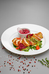 Chicken fillet in bacon with arugula and sauce on a white plate.