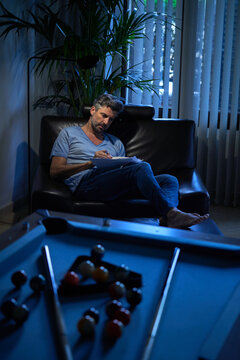 Delighted mature male in casual clothes resting in comfortable armchair and taking notes in notepad