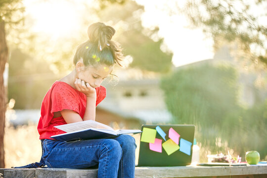 Ten-year-old girl on the field sitting at a wooden table, dressed in a red shirt and jeans