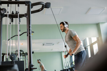 Young athlete strengthening his biceps on exercise machine in a gym.