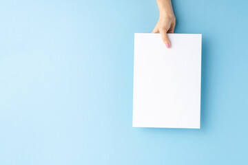 Young female hand showing empty white paper sheet on blue background. Mockup