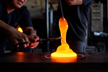 Crop men in workshop cutting piece of hot liquid glass with shears while blowing glass detail