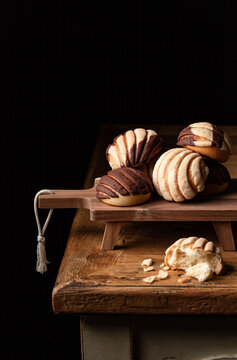 Freshly baked traditional concha bread placed on wooden cutting board on black background