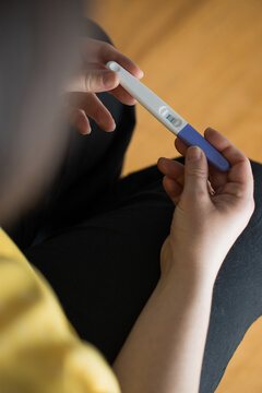 From above of crop unrecognizable female sitting holding pregnancy test with double bars