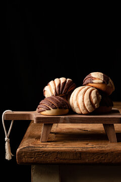 Freshly baked traditional concha bread placed on wooden cutting board on black background