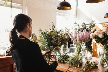 Back view of concentrated female designer arranging decorative blooming bouquets while working on order for event in creative floristry studio
