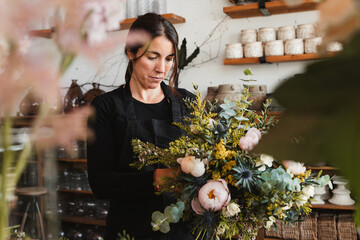 Front view of concentrated female designer arranging decorative blooming bouquets while working on order for event in creative floristry studio