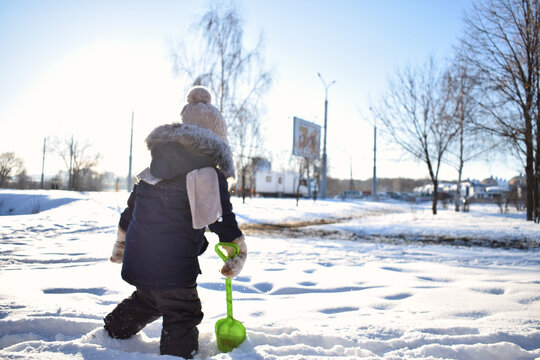 photo of a little boy from the back who plays with snow in winter