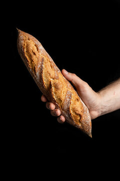 Unrecognizable crop male hand cook holding tasty crunchy baguette in bakery on black background