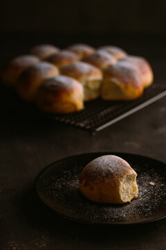 From Above Of Delicious Fresh Round Buns With Soft Texture And Golden Surface Decorated With Powdered Sugar On Cooling Rack And Table On Black Blurred Background