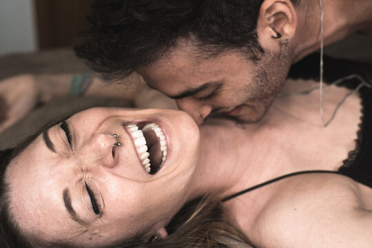 Smiling boyfriend lying on bed and tickling cheerful girlfriend while having fun in bedroom