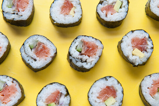 Top view of delicious sushi rolls with rice and salmon placed on colorful yellow table with chopsticks in studio