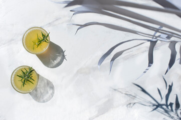 From above of glasses with citrus juice garnished with sprig of rosemary and placed on white marble table on sunny day