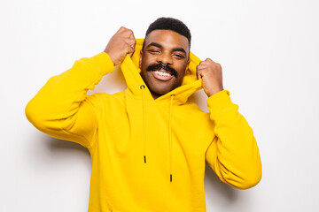 Cheerful black man over white plain background. He is looking at camera and smiling wearing a yellow hoodie
