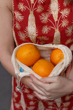 Crop faceless female in summer dress standing with shopping bag with ripe oranges