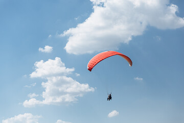 Blue Paraglider flying into the sky with clouds in a sunny day