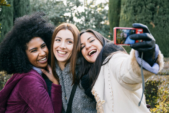 Cheerful female friends taking selfie with camera while standing in park