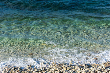 Pebble beach and turquoise water. Texture of water and a pebble. Beach with clear and clear water view from above.