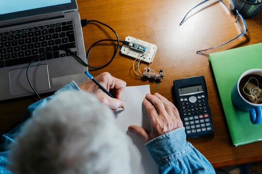 Cropped image of senior man making diagram on paper while repairing laptop at home