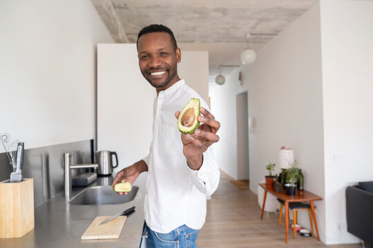 Portrait of smiling man with sliced avocado in his kitchen