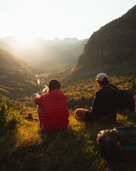 Two young men sitting on the grass watching the sunset on top of a valley in Pyrenees