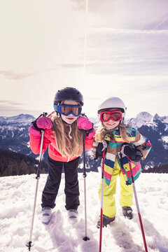Excited sisters with skis standing on snow covered mountain in winter at Spitzingsee, Bavaria, Germany