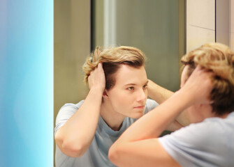 young man looking in the mirror,combing his hair,looking at problems on face