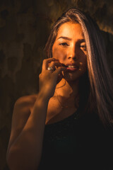 A young Latina brunette leaning against a tree with a slight light on her face. Portrait with a sweet and sensual look